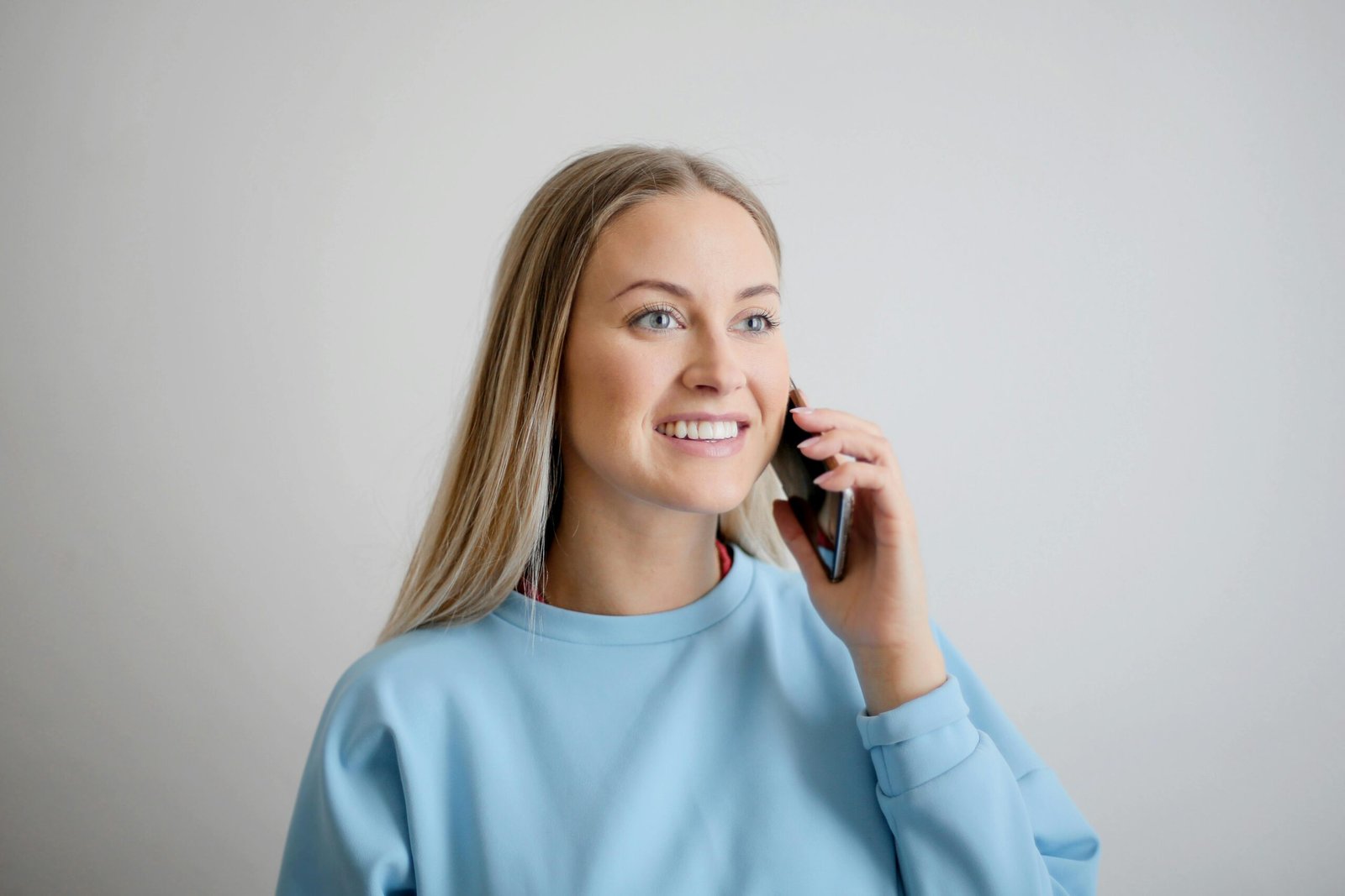 Cheerful woman in blue top smiling while having a conversation on her smartphone.